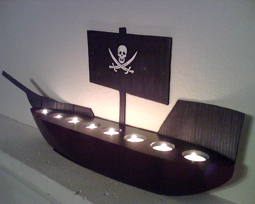 A Dead Man's Chest – candle ship. The black votive holder was found at Goodwill. The back drop is just cardboard painted black. 
								– Richard Russell